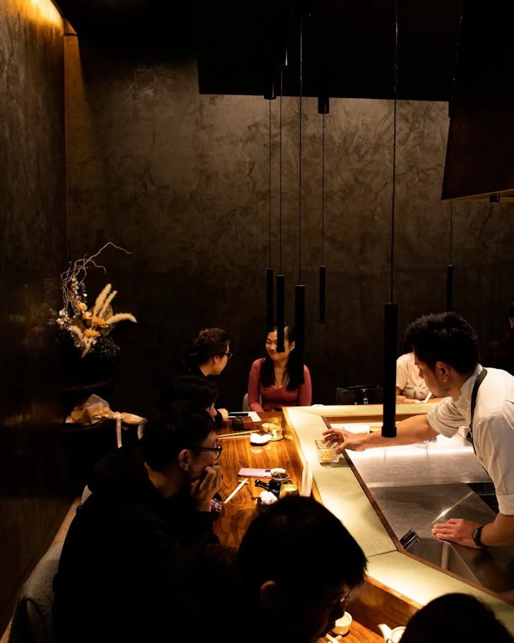 a chef serves tempura over the omakase counter in a concrete restaurant
