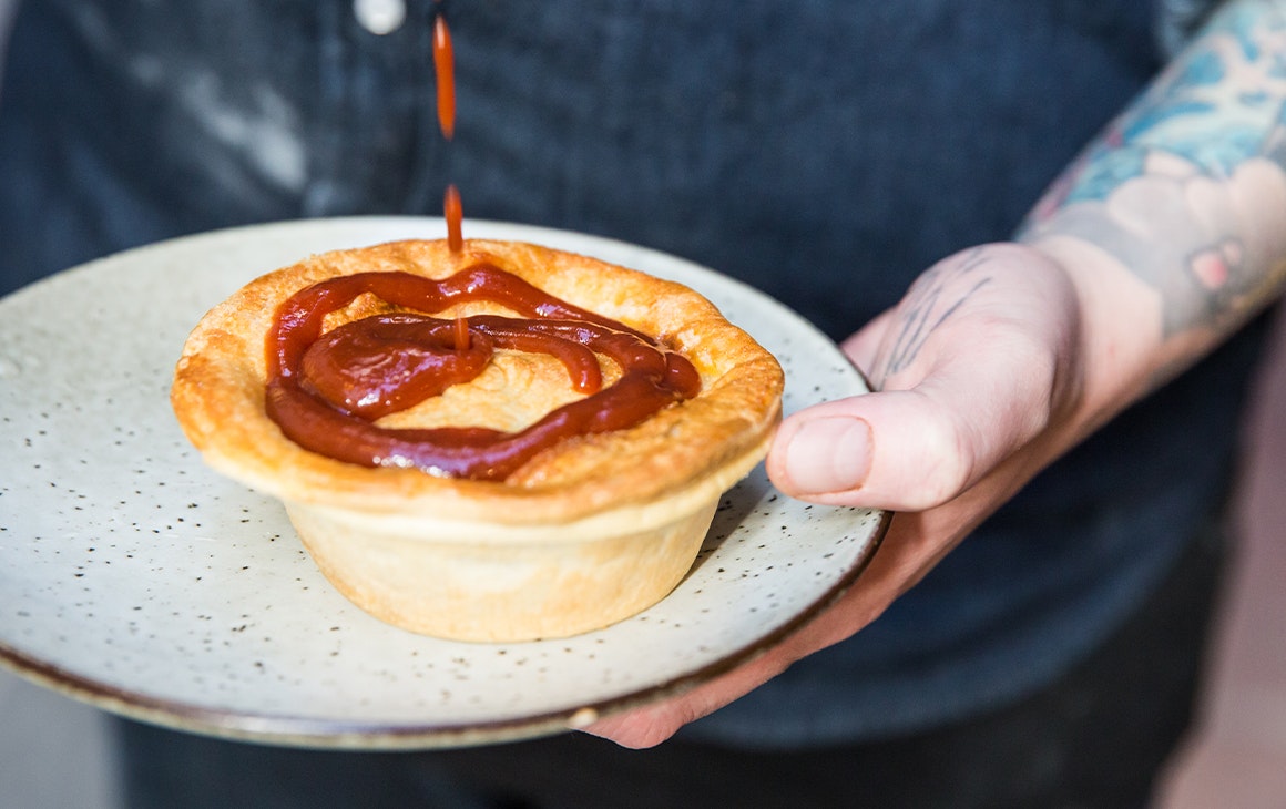 a pie on a plate being topped with tomato sauce