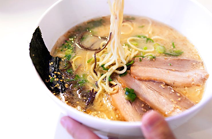 A white bowl of Japanese ramen, topped with pork.