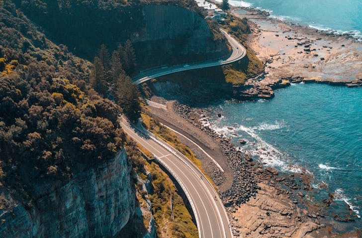 A road snakes through a stunning landscape of blue ocean and rugged cliffs. 