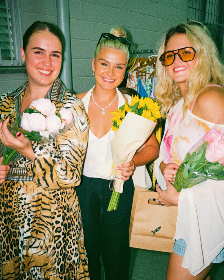 Three market-goers at Sahn Markets holding flowers and clothes.