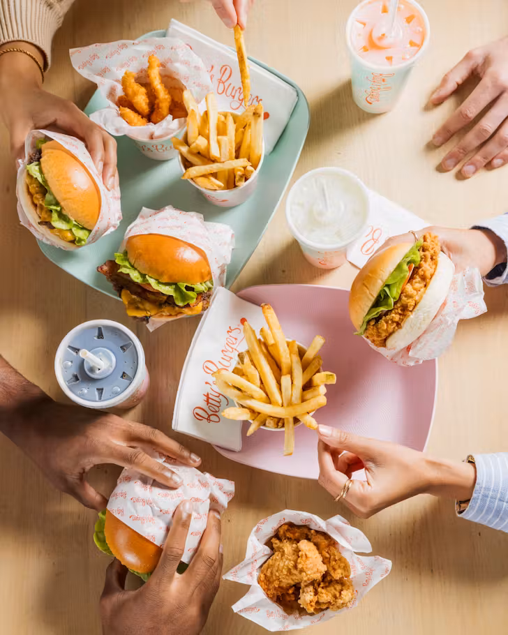 A group of friends enjoys a Betty's burgers spread with burgers, fries and chicken