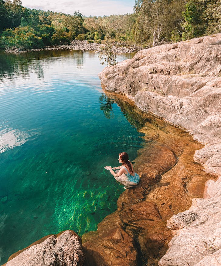a person on the edge of a clear rock pool