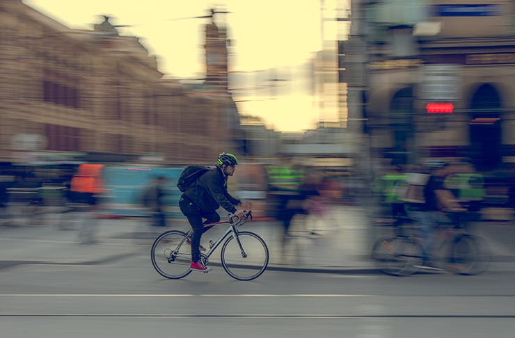 A man riding a bicycle through the intersection of Swanston Street and Flinders Street in Melbourne.