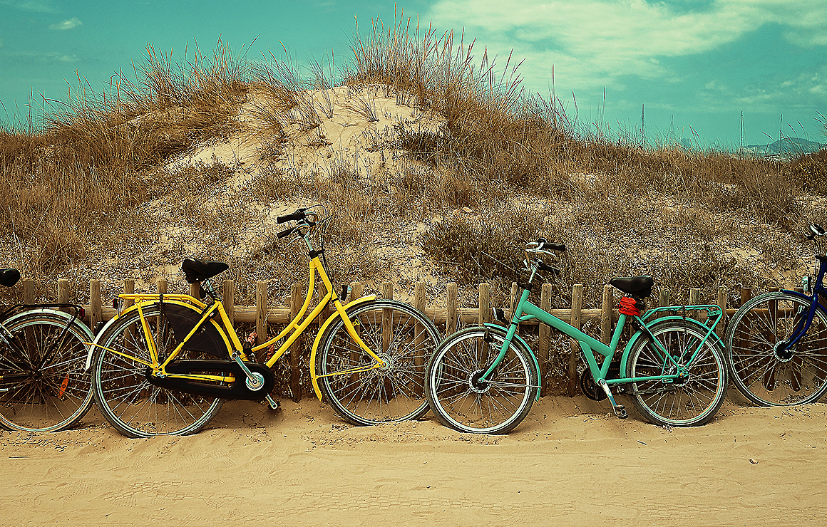 A few bikes parked next to a sand dune under a blue green sky.