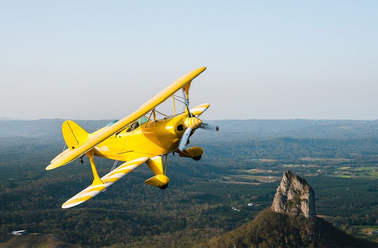 A bright yellow airplane flying over mountains
