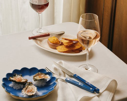 Table set at Bistro Bondi with oysters, pâté, toast and glasses of red and rosé wine, styled with blue-handled cutlery on a crisp white cloth.