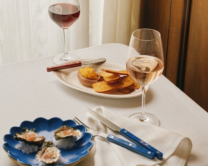 Table set at Bistro Bondi with oysters, pâté, toast and glasses of red and rosé wine, styled with blue-handled cutlery on a crisp white cloth.