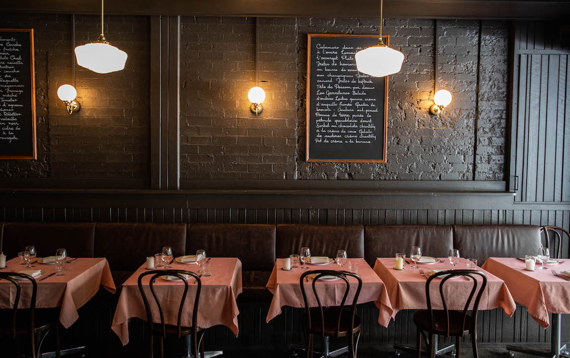 a black dining space with tables topped with pink tablecloths