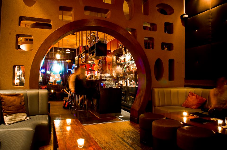 An arched doorway leading to one of the best bars in Melbourne and people drinking at chairs