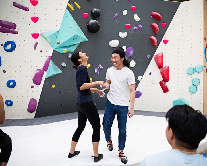 Two people smile and laugh together while standing in front of an indoor bouldering wall.