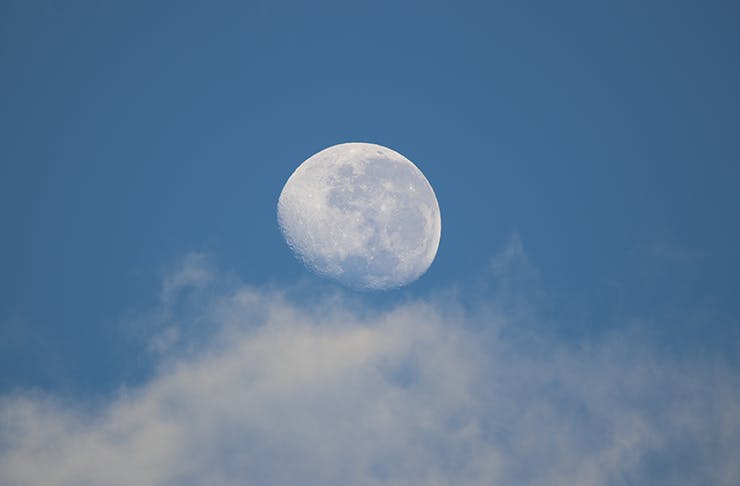 A whitish-blue moon in the mostly clear early evening sky.
