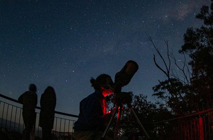A person peering through a telescope on a starry night. 