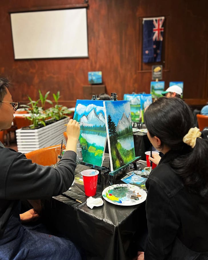 People paint a Bob Ross mountain and lake scene at a Paint & Chill session.