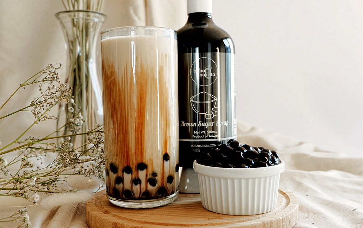 a glass of bubble tea next to a bottle of syrup and a cup of pearls