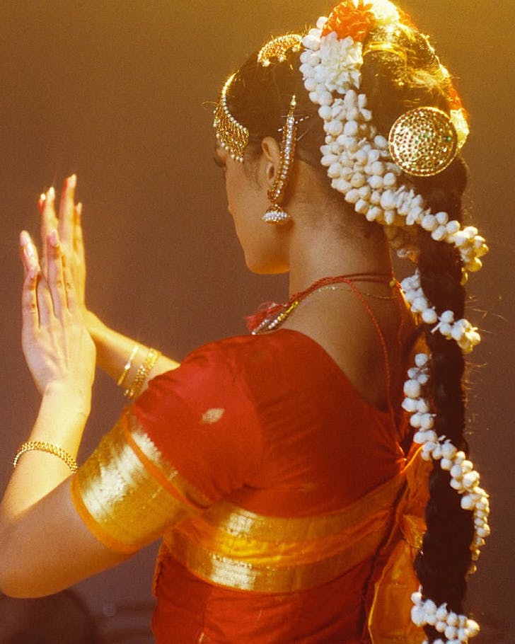Catherine Jessee poses in traditional wear for a glamorous, grainy shot in yellow lighting.