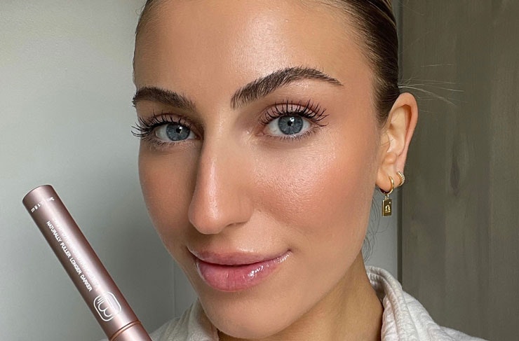A model with glowing skin and fluffy brows holding the Bondi Lash Lab serum. 
