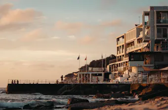 Sunset view of Bondi Beach's shoreline, with the Bondi Icebergs Club overlooking the ocean as waves roll onto the sand.