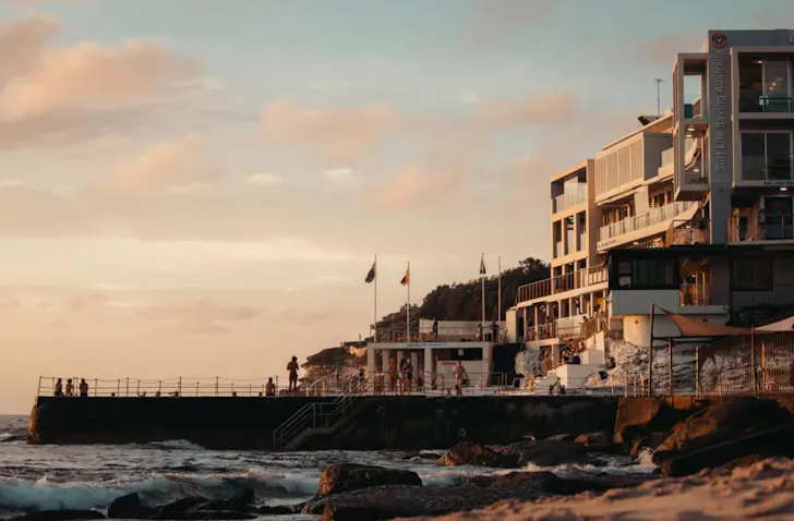 Sunset view of Bondi Beach's shoreline, with the Bondi Icebergs Club overlooking the ocean as waves roll onto the sand.