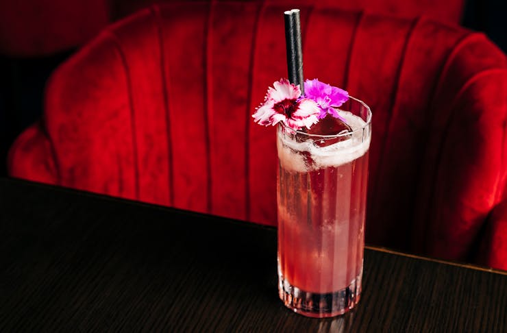a pink cocktail on a table in front of a plush red chair