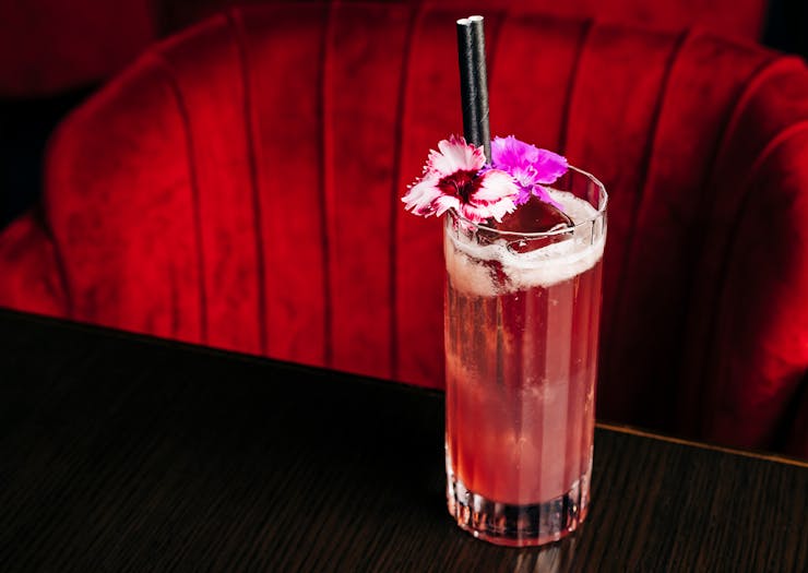 a pink cocktail on a table in front of a plush red chair