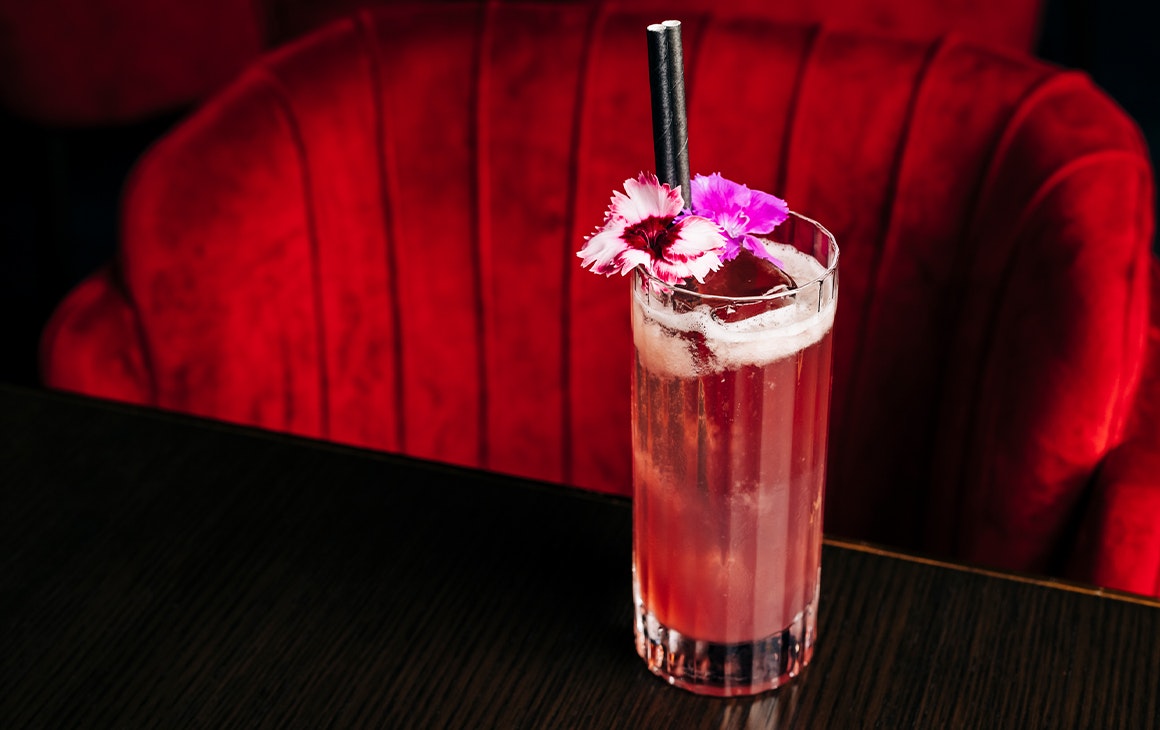 a pink cocktail on a table in front of a plush red chair