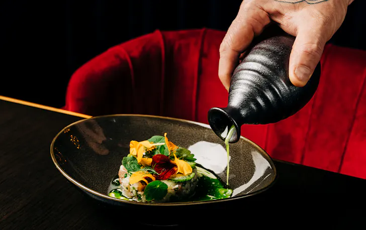 a hand pouring sauce into a plate of tartare