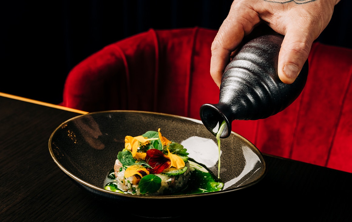 a hand pouring sauce into a plate of tartare