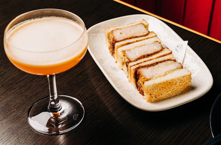 a cocktail beside a plate of pork katsu sandos