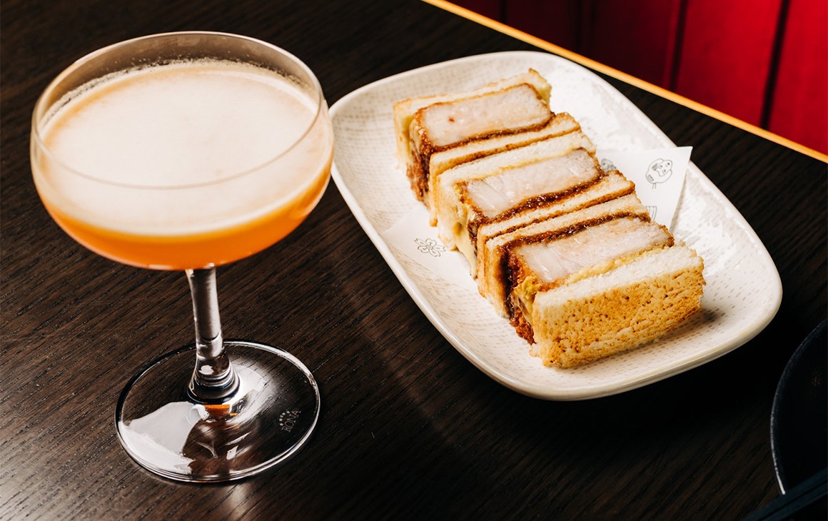 a cocktail beside a plate of pork katsu sandos