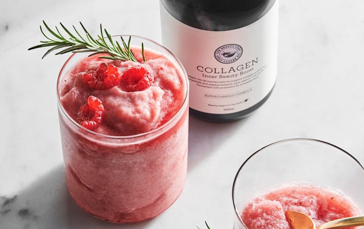 A bottle of The Beauty Chef's supplements next to a glass filled with a raspberry frozen drink