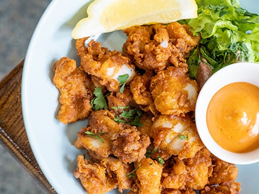 a plate of golden fried calamari with dipping sauce and a lemon wedge