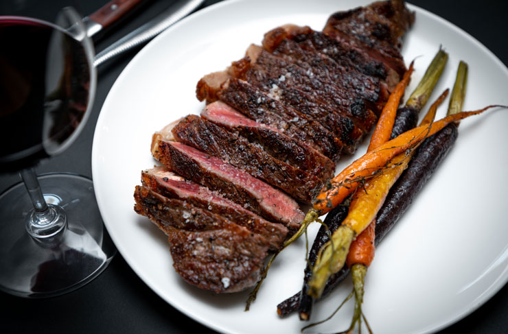 A plate with one of the best steak in Melbourne served alongside carrots and red wine. 
