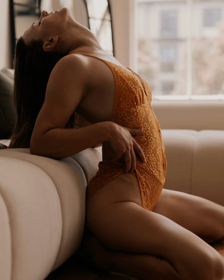 Someone poses sensually in orange lingerie for a Tease Me Boudoir photo shoot.