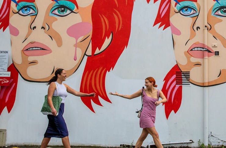 Two girls walk by the Bowie mural in Ghuznee Street, Wellington.