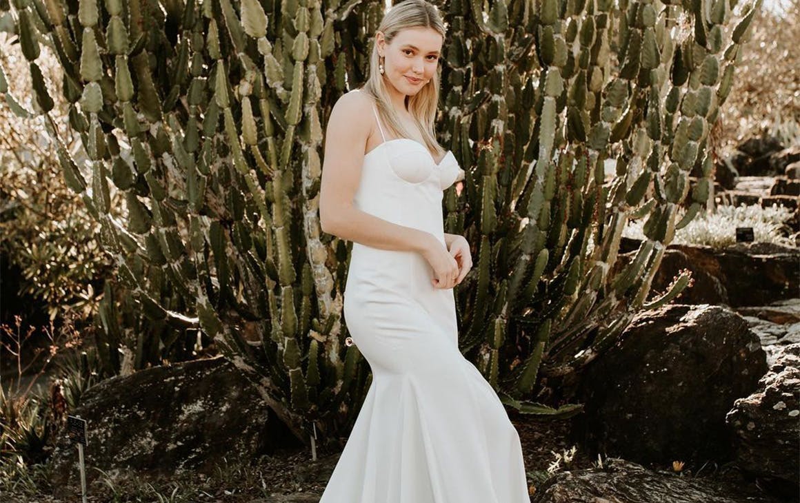 a woman in a wedding dress standing in front of a large cactus