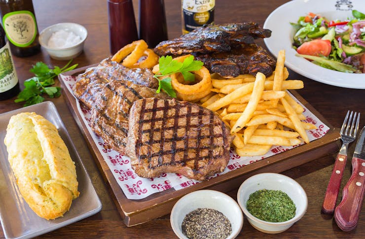 a plate of ribs, steak, chips and sides