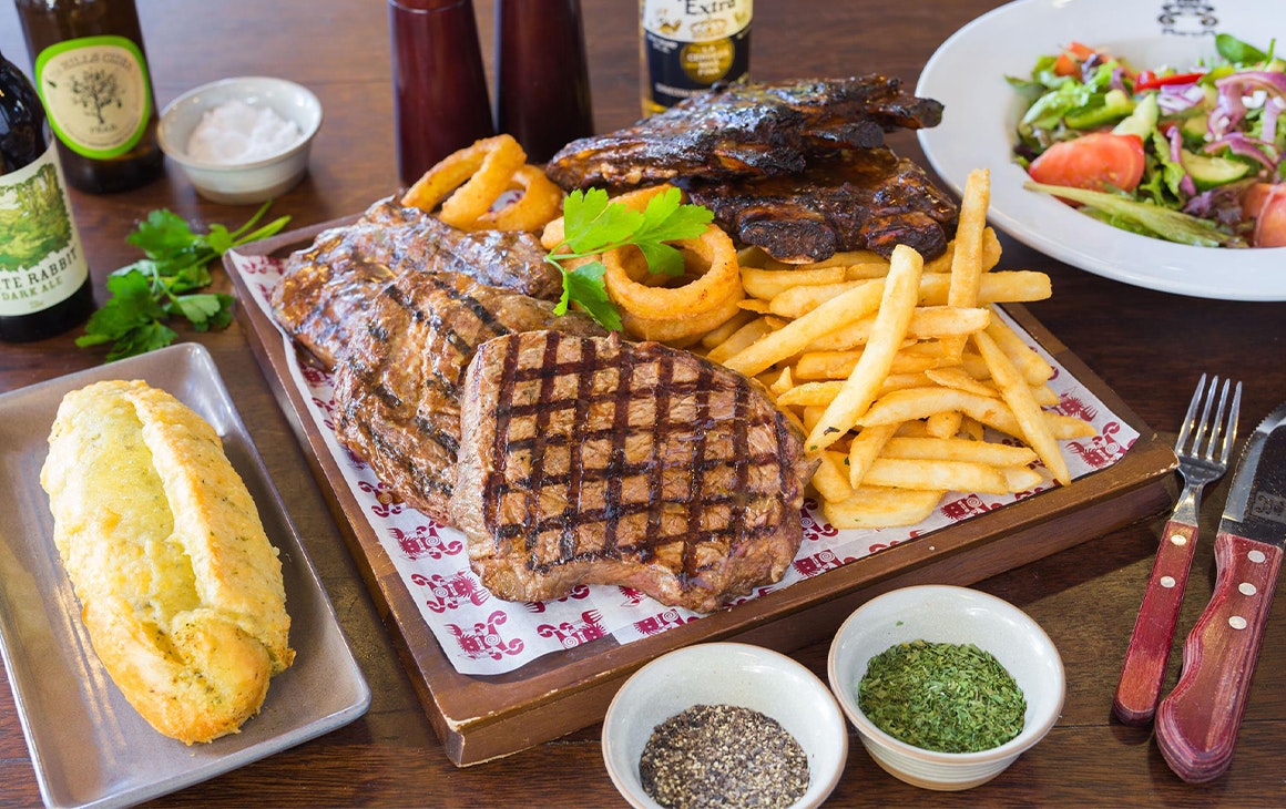 a plate of ribs, steak, chips and sides