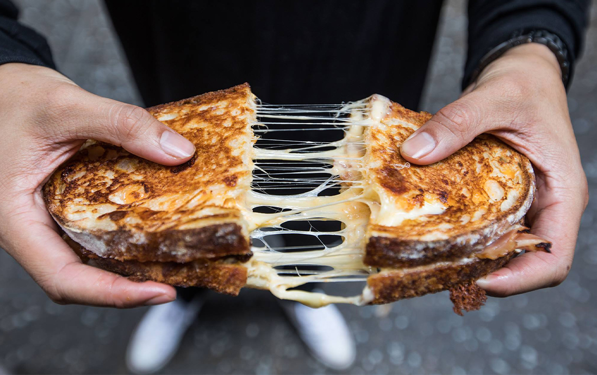 Two hands pulling apart a cheesy toasted sandwich.