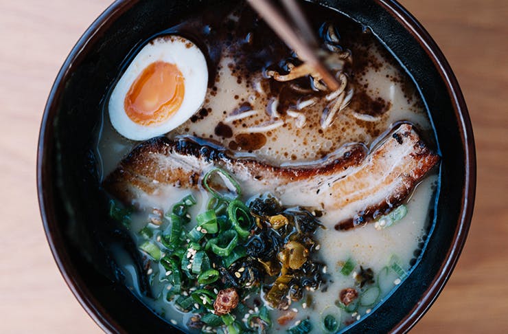 A black bowl of Japanese ramen, topped with pork and a boiled egg.