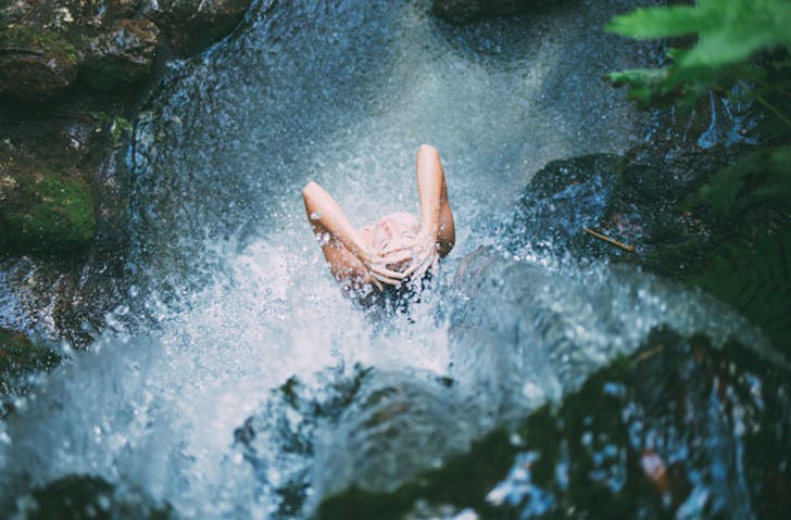 A woman standing beneath a waterfall. 