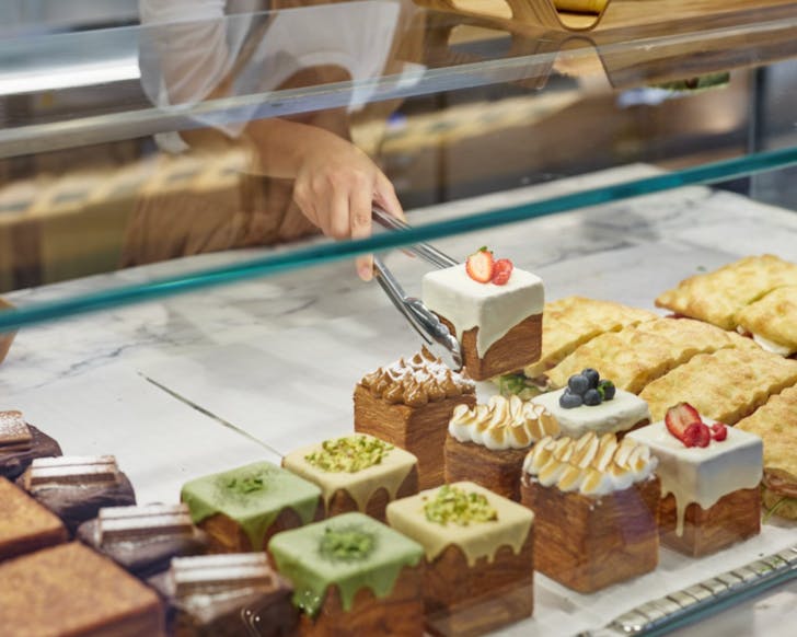 A display window at Buttered of their different tissue bread flavours lined up, including the pistachio flavour that has a light green coat of decorative drip on top with some crushed pistachios sprinkled. 