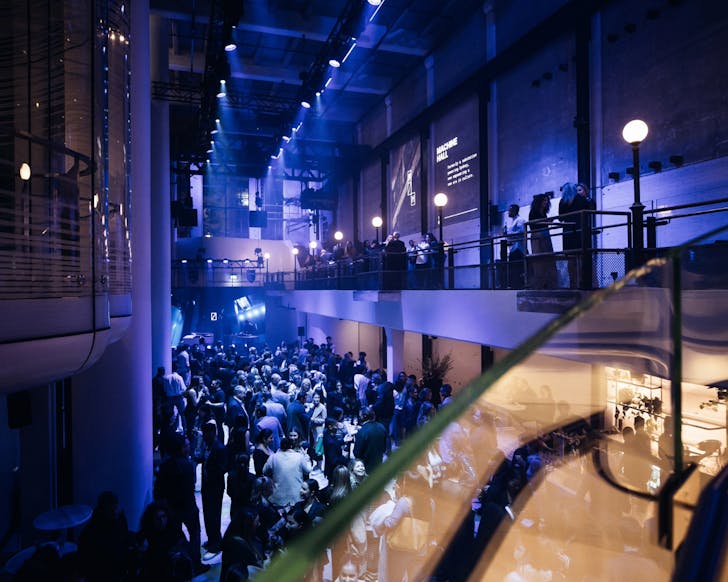 A wide shot of the interior of Machine Hall, lit up in a moody atmosphere with colourful blue lighting and filled with many people.
