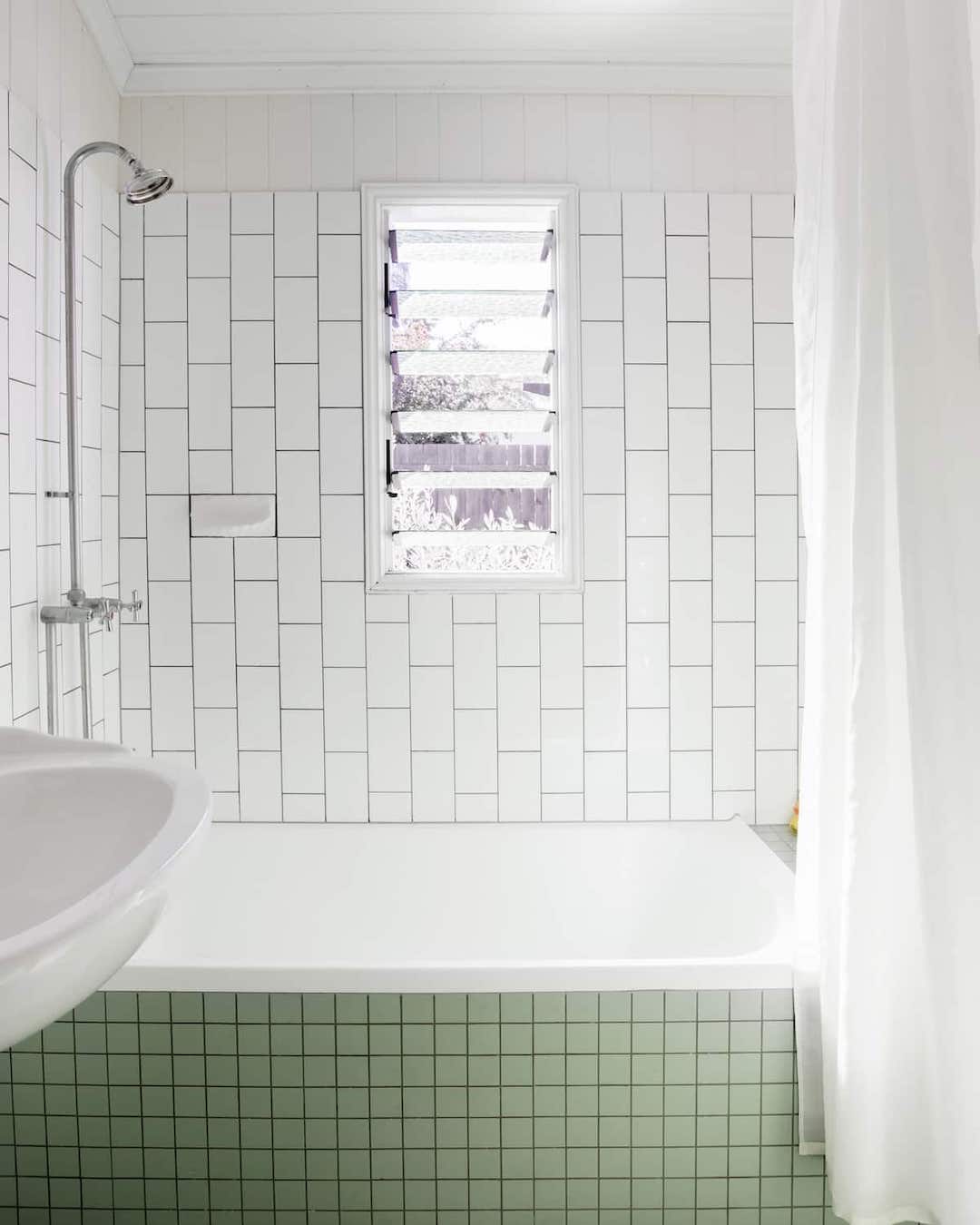 A pastel green-tiled bathtub set amongst white tonge-and-groove walls.