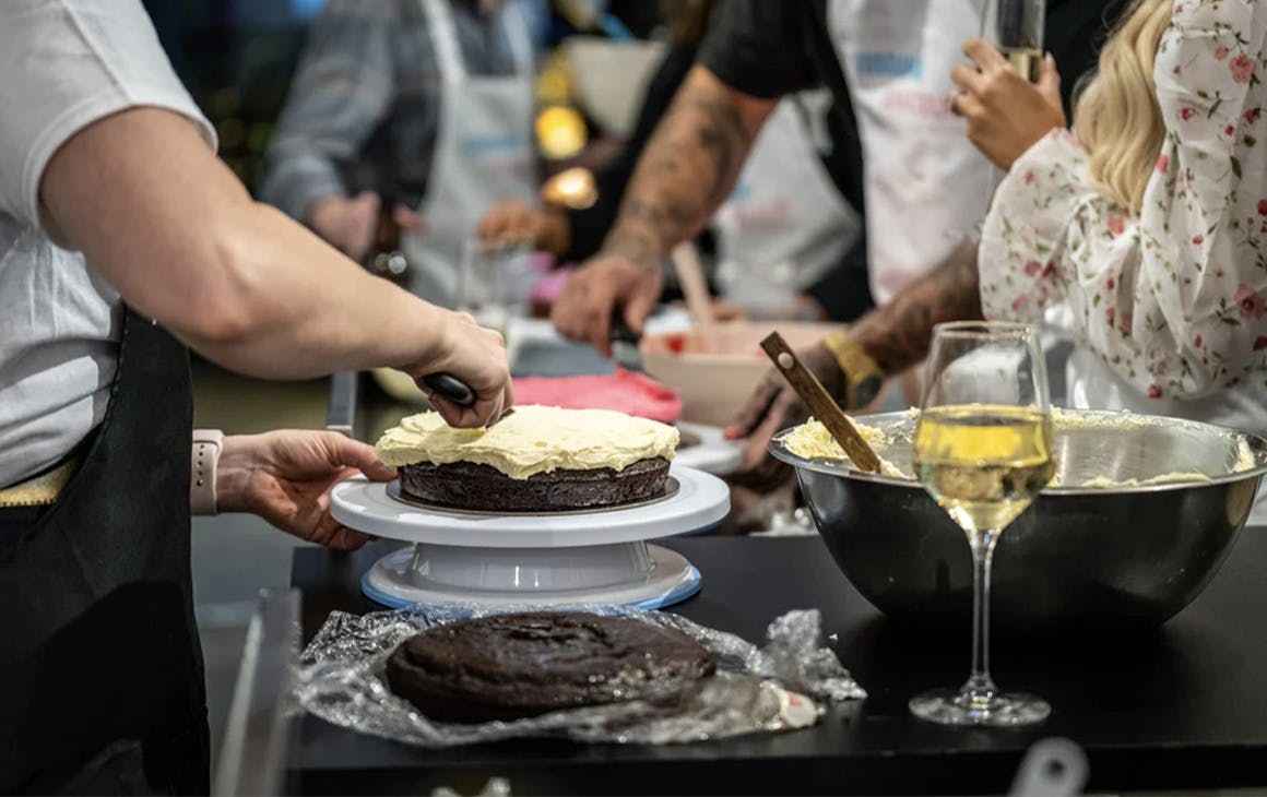 a person icing a cake with a glass of wine nearby