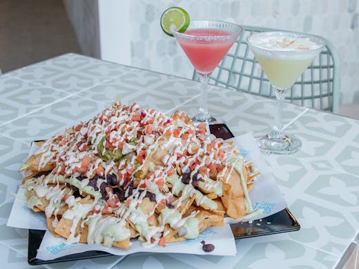 huge plate of nachos with two cocktails
