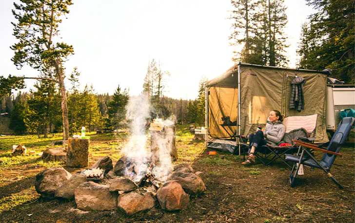 a woman by a tent near a campfire
