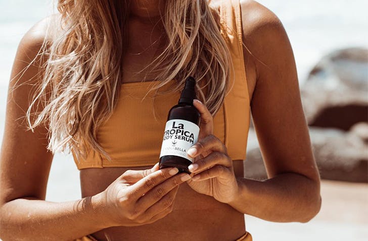 a woman in a yellow bikini holding a skin serum bottle