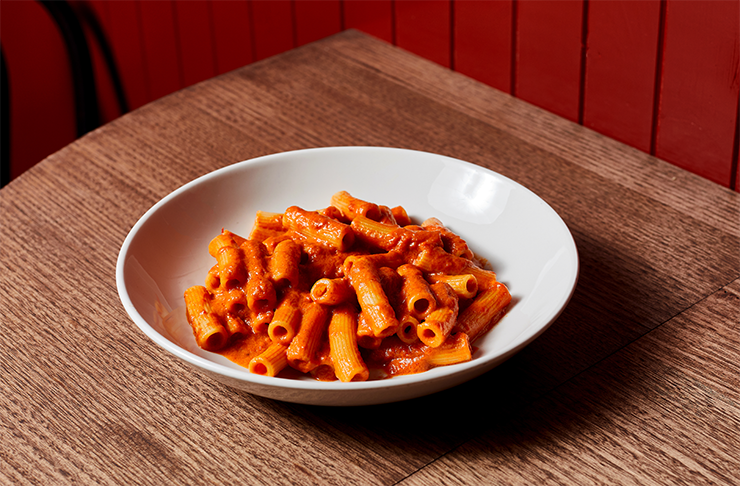 A bowl of pasta and red sauce on a wooden table.