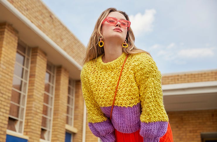 A woman in a colourful knitted sweater looking up at the sky.